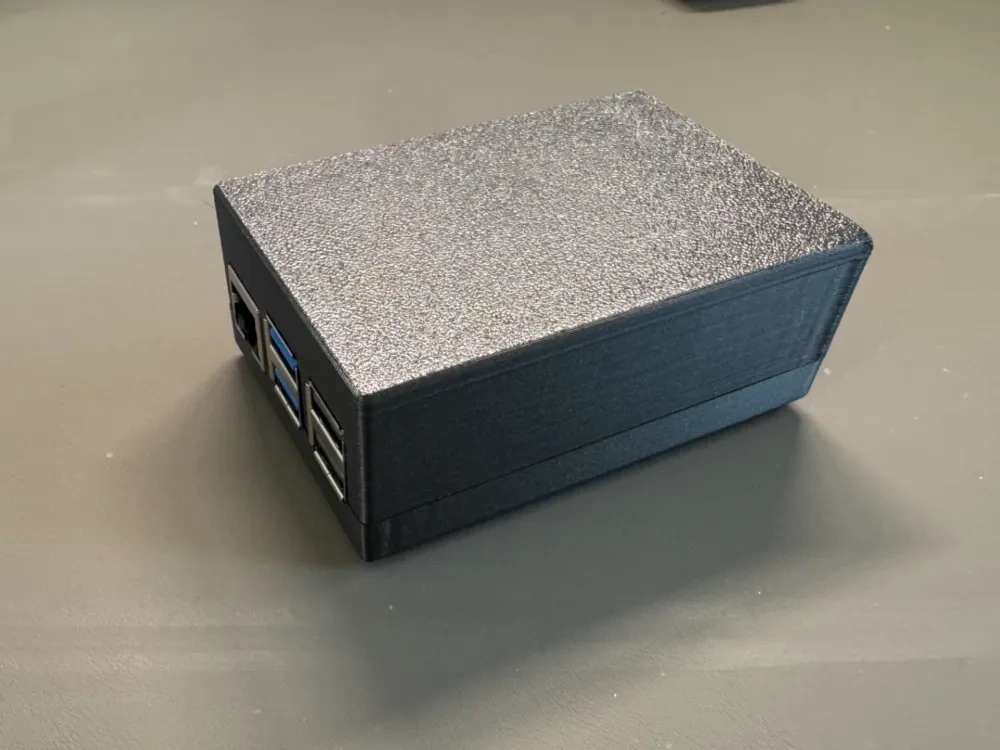 A closed black 3D printed case for a Raspberry Pi 5 with its USB and Ethernet ports exposed.